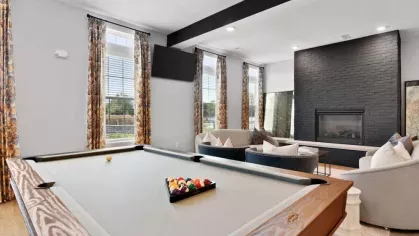A stylish recreation area featuring a full-sized pool table, a large black brick fireplace, and elegant lounge seating.