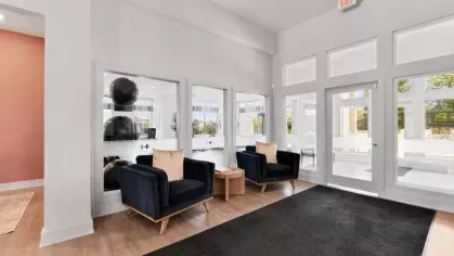 A welcoming seating area with two navy armchairs and beige pillows, overlooking the fitness center through large glass windows.