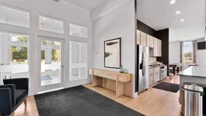 A bright entryway with large windows and a modern wooden console table leading into the kitchen and lounge area.