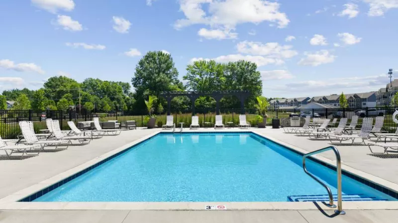 A large outdoor pool surrounded by comfortable seating, lush landscaping, and a picturesque neighborhood setting.