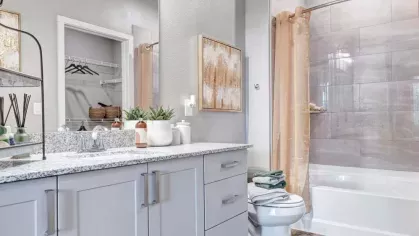 A modern bathroom with a double vanity, granite countertops, and a sleek white cabinet design, featuring a glass shower with large tiled walls.