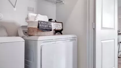 A well-organized laundry room with a washer and dryer, floating shelves, and charming decorative signs for a functional and stylish space.