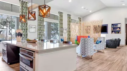 Stylish community lounge with a gourmet kitchen, pendant lighting, and contemporary seating, designed for social gatherings and resident events.