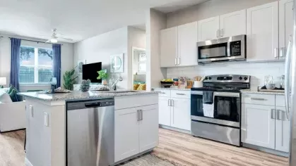 A luxury kitchen with stainless steel appliances, white shaker cabinets, and a large center island with bar seating, seamlessly opening into the living area.