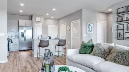 Open-concept living area with a modern white couch, a stylish coffee table, and a view into the contemporary kitchen with a breakfast bar.
