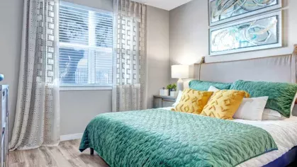 A serene bedroom featuring a plush green bedspread, yellow accent pillows, and elegant wall art, creating a cozy and stylish retreat.