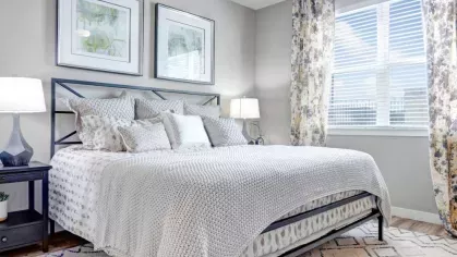 A sophisticated bedroom with a soft gray and white color palette, complete with a textured duvet, modern artwork, and large windows allowing natural light.
