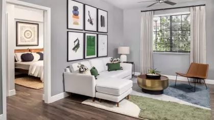 A sophisticated living room with a white sectional, abstract artwork, and a cozy reading chair, leading to a stylish bedroom at Locklyn West Palm.