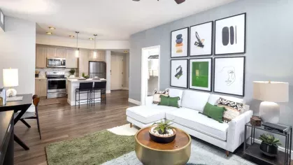 A bright and inviting living space with a minimalist aesthetic, featuring a neutral-toned sofa, bold wall art, and a modern open-concept kitchen.