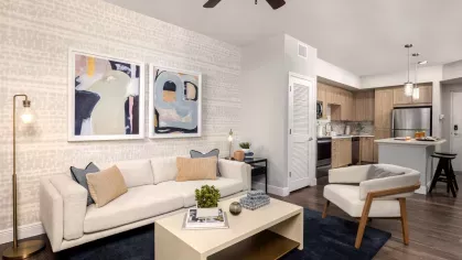 A stylish living space featuring a neutral-toned sofa, artistic wall decor, and floor-to-ceiling windows that bring in natural light.