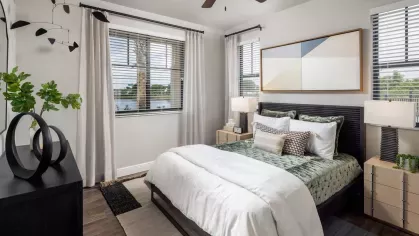 A stylish bedroom featuring a modern bed frame, plush textiles, and large windows with scenic views of palm trees and water.