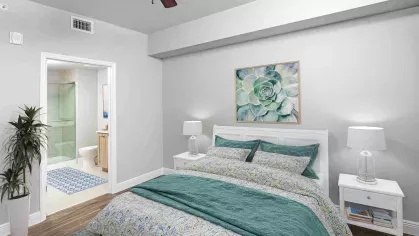 Spacious bedroom featuring a luxurious green velvet bedspread, elegant geometric artwork, and an adjoining walk-in closet. Modern lighting and stylish nightstands complete the space.