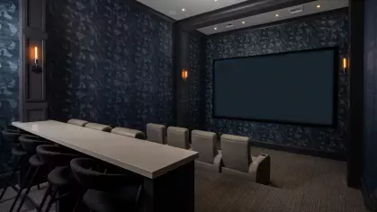 A luxurious private theater at Locklyn West Palm Apartments, featuring plush recliner seating, a large projection screen, and elegant dark blue decor with ambient lighting.