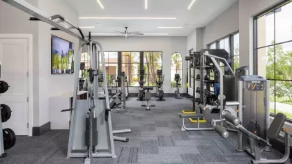 A state-of-the-art fitness center with floor-to-ceiling windows, featuring strength training equipment, TRX bands, medicine balls, and modern exercise machines.