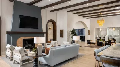 A spacious lounge area with a striking fireplace, high wooden beams, plush seating, and large windows bringing in natural light.