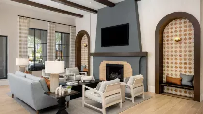 A spacious lounge area with a striking fireplace, high wooden beams, plush seating, and large windows bringing in natural light.