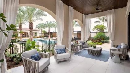 A beautifully designed outdoor patio with stylish white armchairs, a coffee table, and pool views framed by flowing white curtains.