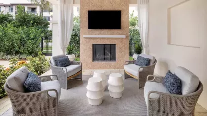 A stylish outdoor seating area at Locklyn West Palm featuring cozy armchairs, a built-in fireplace, and a mounted TV, perfect for relaxation.