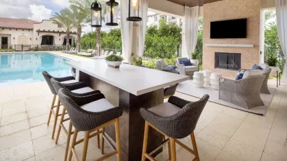 A modern outdoor bar with high-top seating and a cozy fireplace seating area, creating the ultimate entertainment space by the pool.