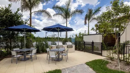 A serene outdoor grilling and dining space with blue umbrellas, surrounded by lush greenery and overlooking a beautiful lake.