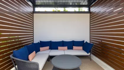 A contemporary outdoor cabana featuring a comfortable sectional sofa with navy and coral accent pillows, perfect for unwinding.
