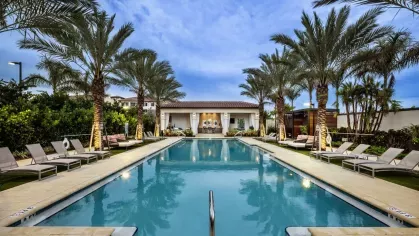 A luxurious swimming pool lined with palm trees and sun loungers, leading to a stylish poolside lounge with cabana seating at Locklyn West Palm Luxury Apartments.