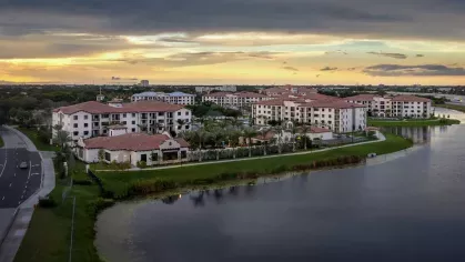 A breathtaking sunset over Locklyn West Palm Luxury Apartments, with the lake reflecting the sky's warm hues and the community’s architecture blending harmoniously with nature.