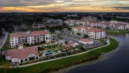 A stunning aerial shot of Locklyn West Palm Luxury Apartments at dusk, showcasing Mediterranean-style buildings, lush landscaping, and a resort-style pool by the lake.