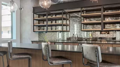 Sleek bar area with a mirrored backsplash, industrial-style stools, and exposed ductwork.