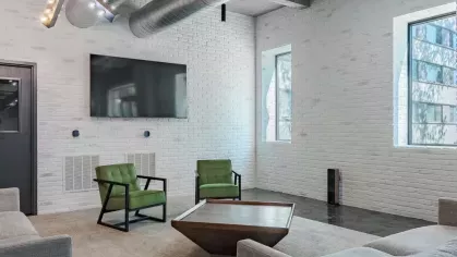 Cozy room with green accent chairs, a large TV, and exposed industrial ceilings.