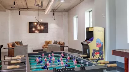 Game room with foosball table, arcade game, and cozy seating in a bright space.