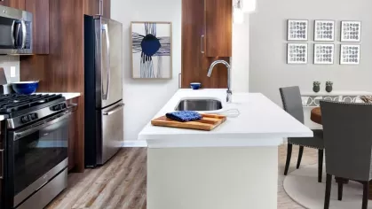A contemporary kitchen with stainless steel appliances, wood cabinetry, and a quartz countertop island, leading into a stylish dining area.