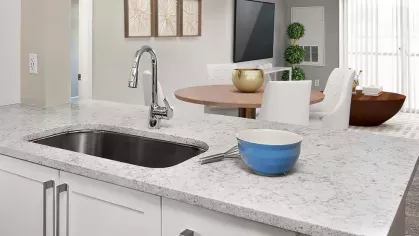 A sleek, open-concept kitchen with a modern white quartz island, pendant lighting, and a dining area with contemporary furnishings.