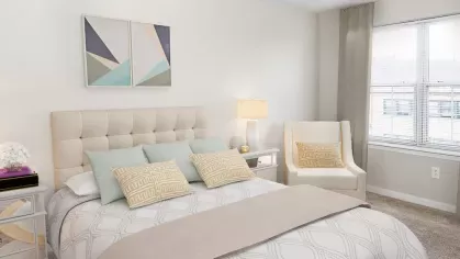 A bright and spacious bedroom with a plush, tufted headboard, elegant neutral-toned bedding, and modern décor at The Mark at Mamaroneck Luxury Apartments.
