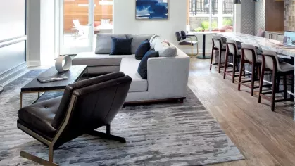 A modern resident lounge with plush seating, a stylish area rug, and a sleek marble-topped bar with pendant lighting, creating a warm and inviting communal space.