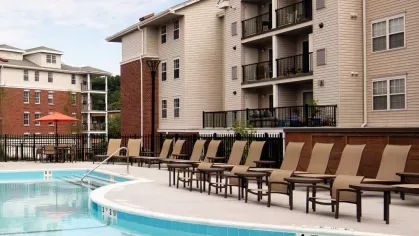 A resort-style swimming pool with ample lounge chairs, tables, and red umbrellas, surrounded by modern apartment buildings at The Mark at Mamaroneck.