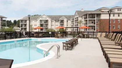 A resort-style swimming pool with ample lounge chairs, tables, and red umbrellas, surrounded by modern apartment buildings at The Mark at Mamaroneck.