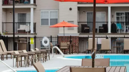 Close-up of a vibrant red umbrella shading a poolside dining table, set against the backdrop of stylish apartment balconies.