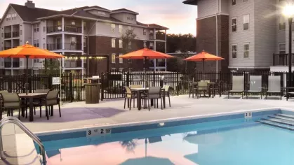 A stunning sunset over the pool area, reflecting soft colors in the water, with orange umbrellas and lounge chairs for relaxation.