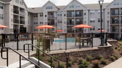 A well-landscaped entrance to the pool area with a black fence, brick pathways, and vibrant greenery enhancing the surroundings.
