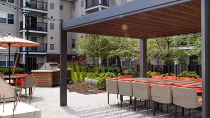 A stylish pergola-covered dining area with woven chairs, orange cushions, and a long table for gatherings.