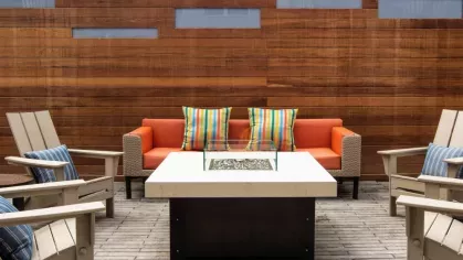 A modern outdoor fire pit surrounded by cushioned sofas and Adirondack chairs, creating a warm and inviting social space.