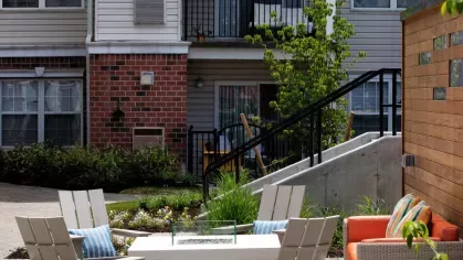 A beautifully landscaped courtyard featuring a communal fire pit, comfortable chairs, and direct access to luxury apartment balconies.