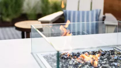 A contemporary fire pit with glass paneling and reflective stones, creating a warm ambiance in the luxury apartment’s outdoor lounge.
