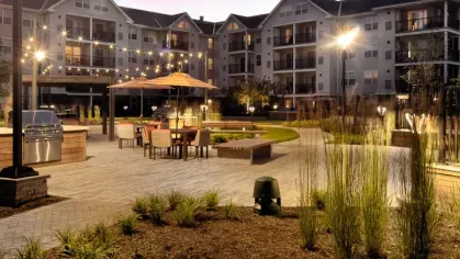 A beautifully landscaped courtyard featuring elegant outdoor seating, grilling stations, and string lights illuminating the space at twilight.
