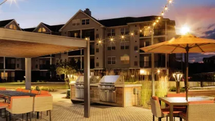 A well-lit communal outdoor space with modern grilling stations, a covered dining area, and ambient string lighting for an inviting evening setting.