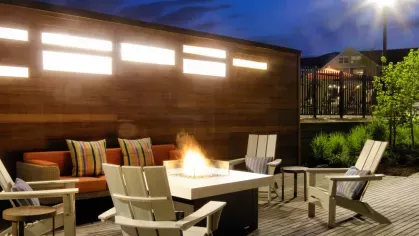 A stylish outdoor lounge featuring a fire pit surrounded by Adirondack chairs and a cozy seating area with decorative cushions against a warm wooden accent wall.