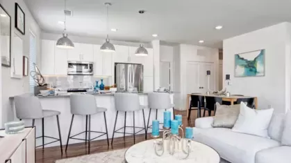 A stylish open-concept kitchen and living area with white cabinetry, stainless steel appliances, and a chic marble coffee table.