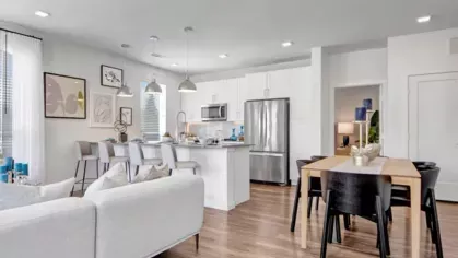A spacious apartment interior featuring a kitchen island with barstools, a dining table, and a cozy living room with modern decor.