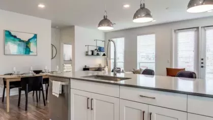 A spacious kitchen with a waterfall island, pendant lights, and a dining area in the background.
